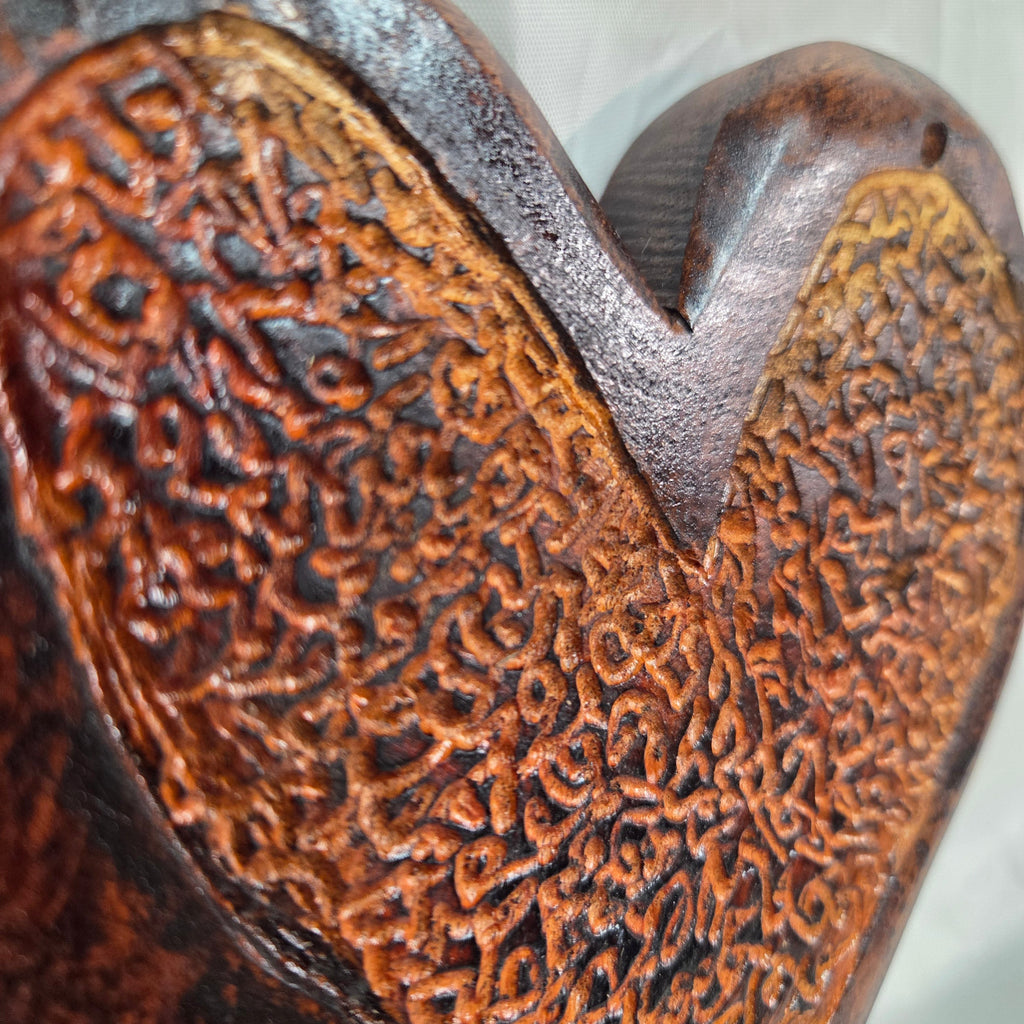 A heart-shaped wooden hanging heart with a highly textured, carved pattern on the interior, photographed on a wrinkled white fabric background.