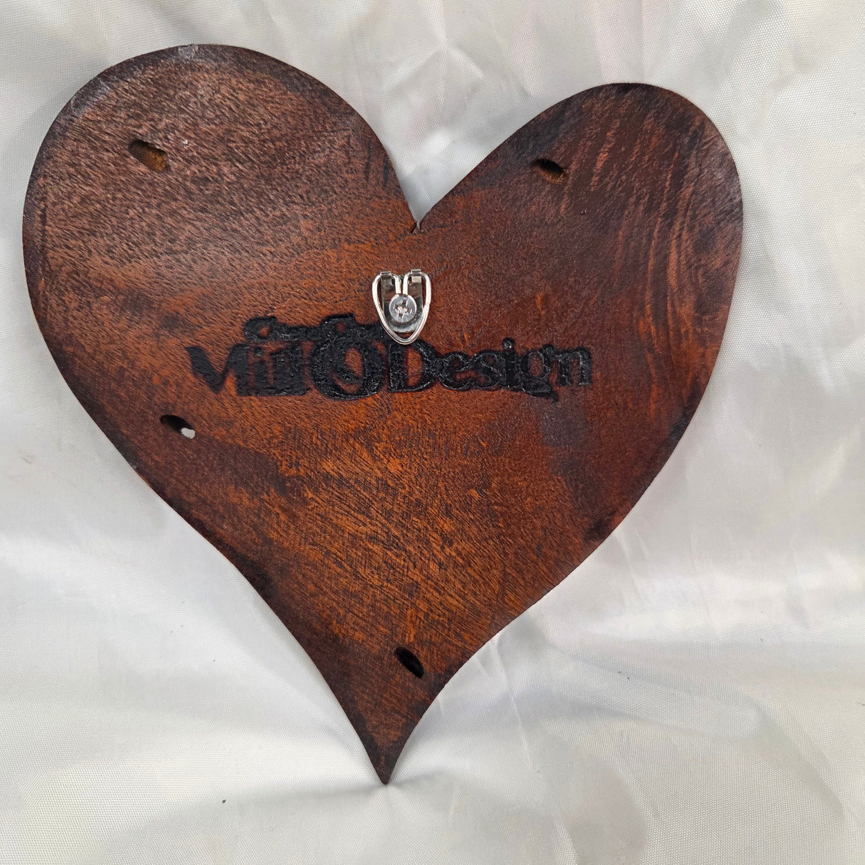 A heart-shaped wooden hanging heart with a highly textured, carved pattern on the interior, photographed on a wrinkled white fabric background.