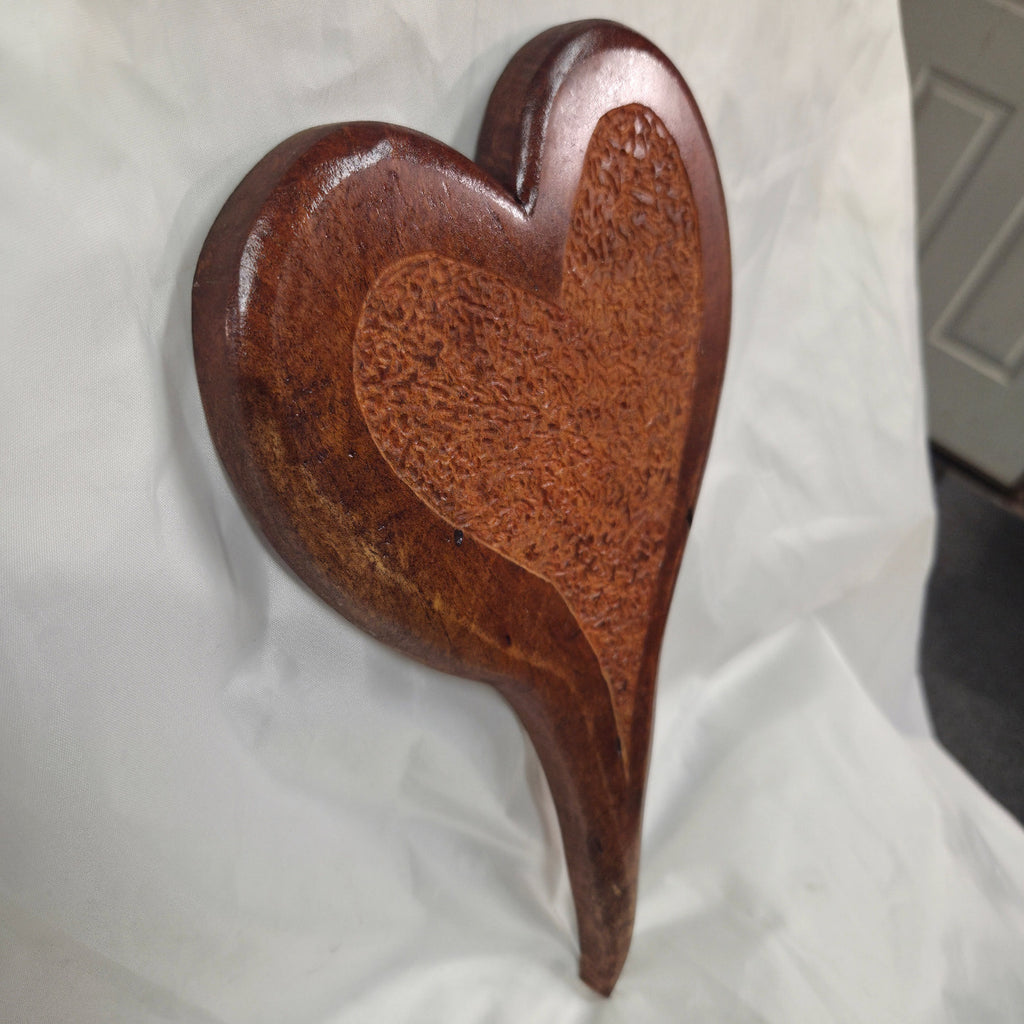A heart-shaped Mesquite Hanging heart wall art with Hand carved center section with a glossy dark reddish-brown finish and a textured lighter wood inlay, displayed on a draped white fabric backdrop.