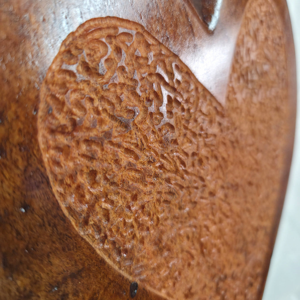 Close-up of a carved wooden object with a textured, organic leaf-like pattern in warm medium brown tones.