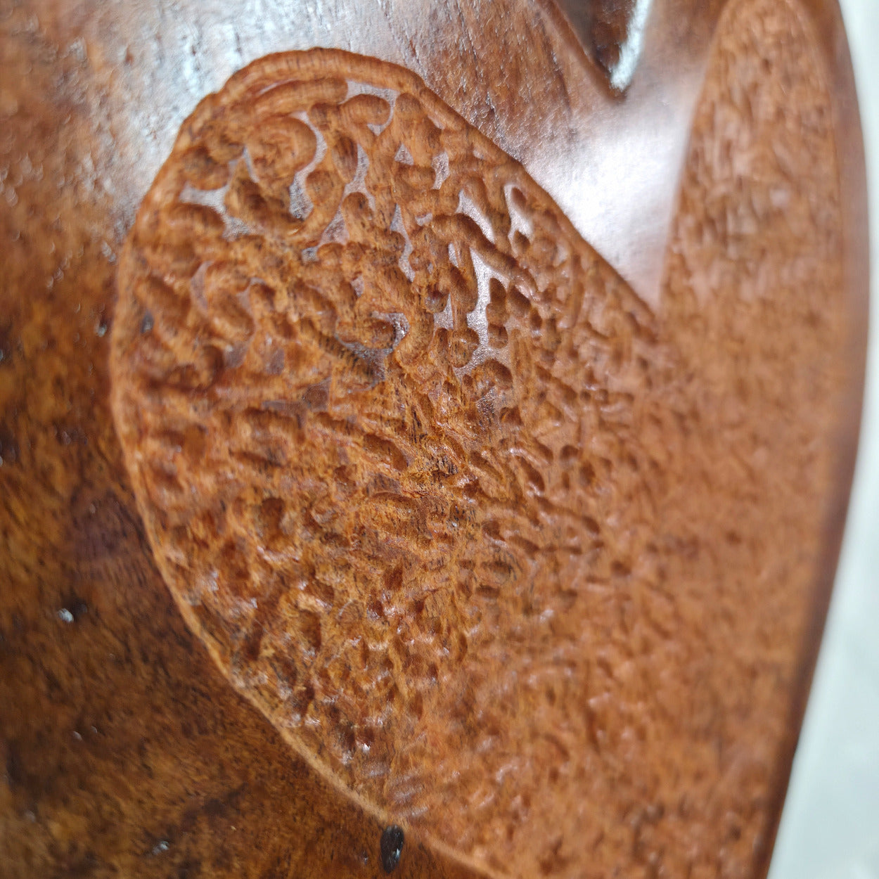 Close-up of a carved wooden object with a textured, organic leaf-like pattern in warm medium brown tones.