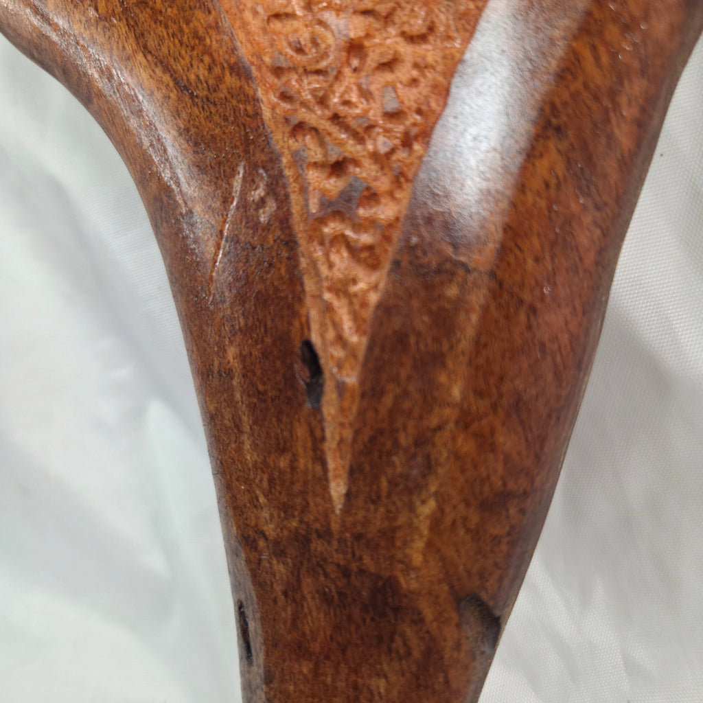 Close-up of a carved wooden object, showing rich brown wood grain, a textured carved panel, and a glossy finish against a white fabric background.