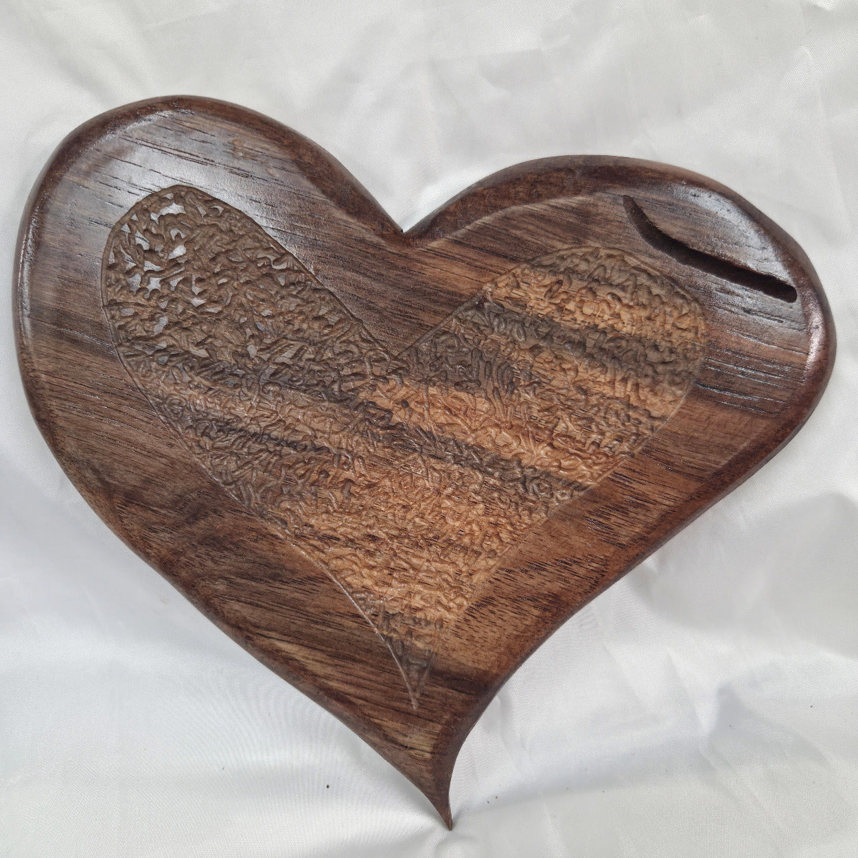 A hand carved heart-shaped White Oak Hanging heart wall art with a carved pattern in the center, photographed on a wrinkled white background.