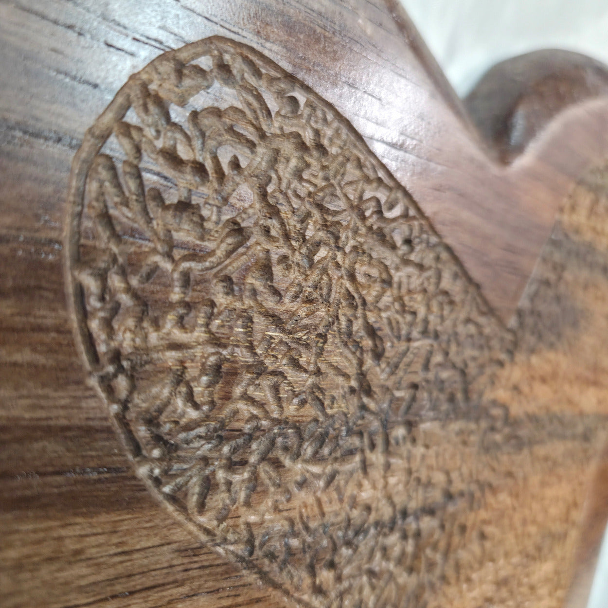 Close-up of a carved wooden object with intricate floral or scroll-like relief detailing on a brown wood-grain surface.