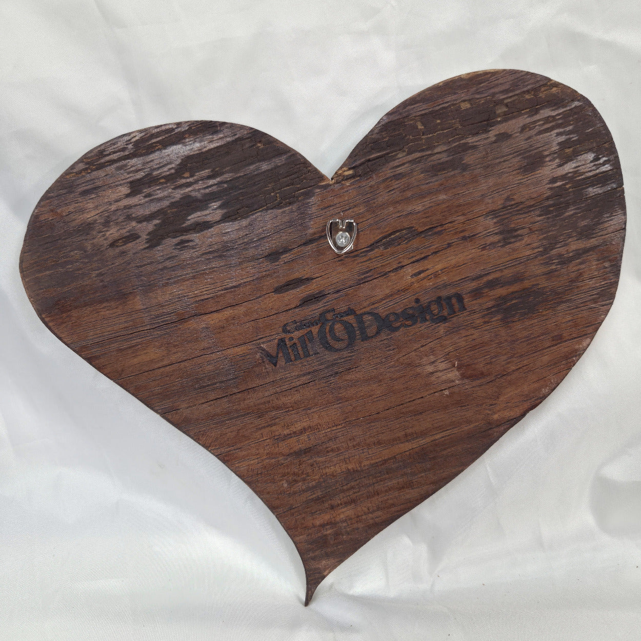 A hand carved heart-shaped White Oak Hanging heart wall art with a carved pattern in the center, photographed on a wrinkled white background.