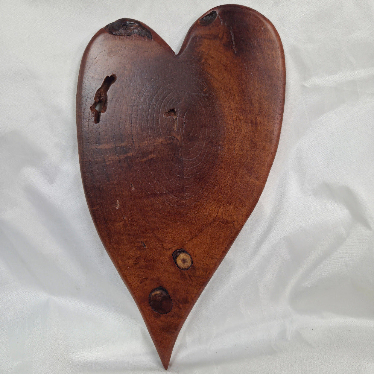 A heart-shaped Mesquite wall plaque with natural live edges and visible wood grain, displayed on a wrinkled white fabric background.