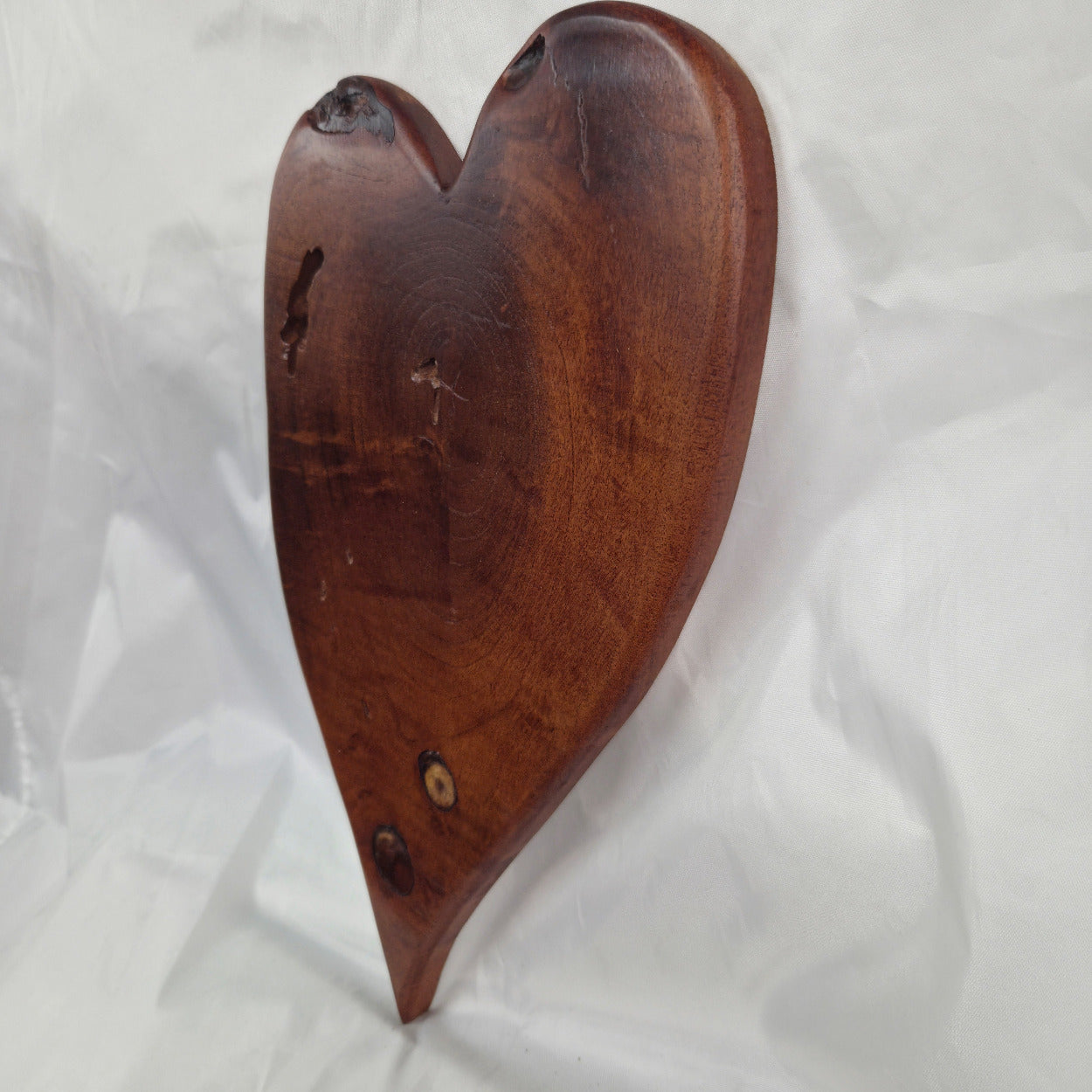 A heart-shaped Mesquite wall plaque with natural live edges and visible wood grain, displayed on a wrinkled white fabric background.