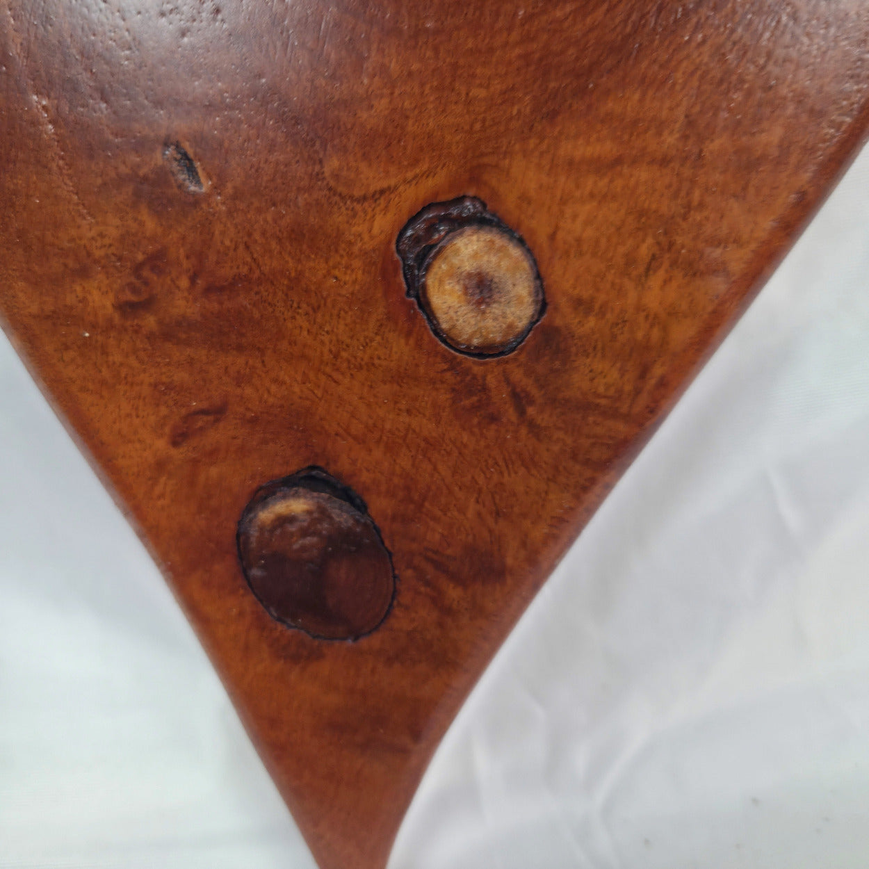 Close-up of a mesquite hanging heart with two dark circular defects or knots on a white background.