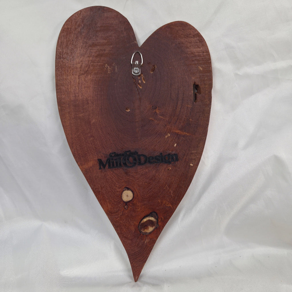 A heart-shaped Mesquite wall plaque with natural live edges and visible wood grain, displayed on a wrinkled white fabric background.