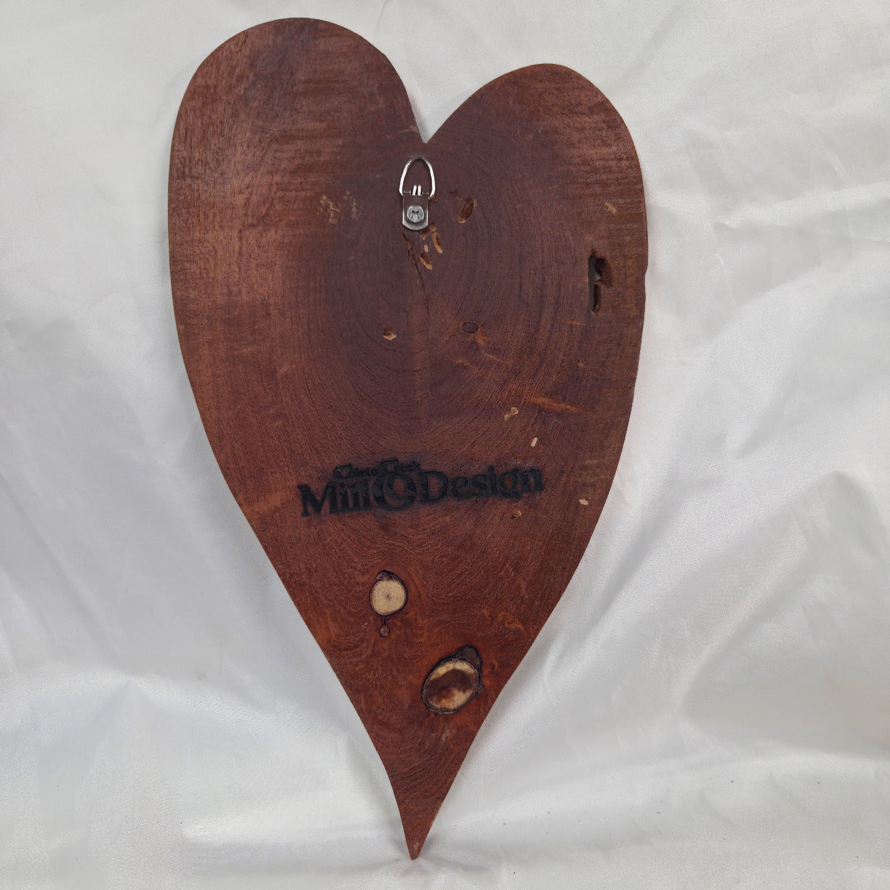 A heart-shaped Mesquite wall plaque with natural live edges and visible wood grain, displayed on a wrinkled white fabric background.