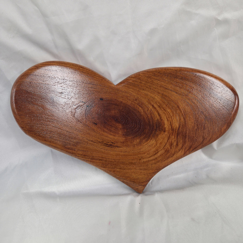 A heart-shaped hanging heart wall are with a glossy finish and visible wood grain, placed on a wrinkled white fabric background.