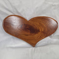 A heart-shaped hanging heart wall are with a glossy finish and visible wood grain, placed on a wrinkled white fabric background.