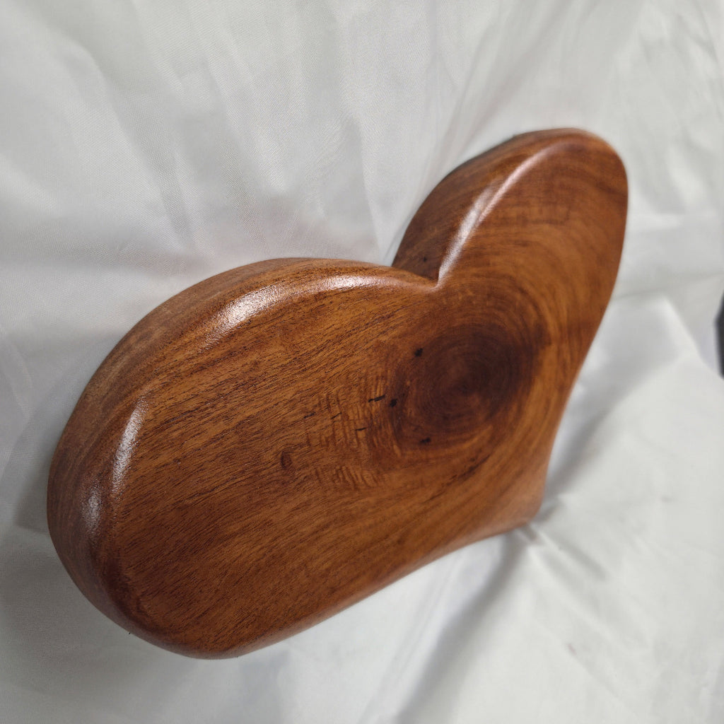 A heart-shaped hanging heart wall are with a glossy finish and visible wood grain, placed on a wrinkled white fabric background.