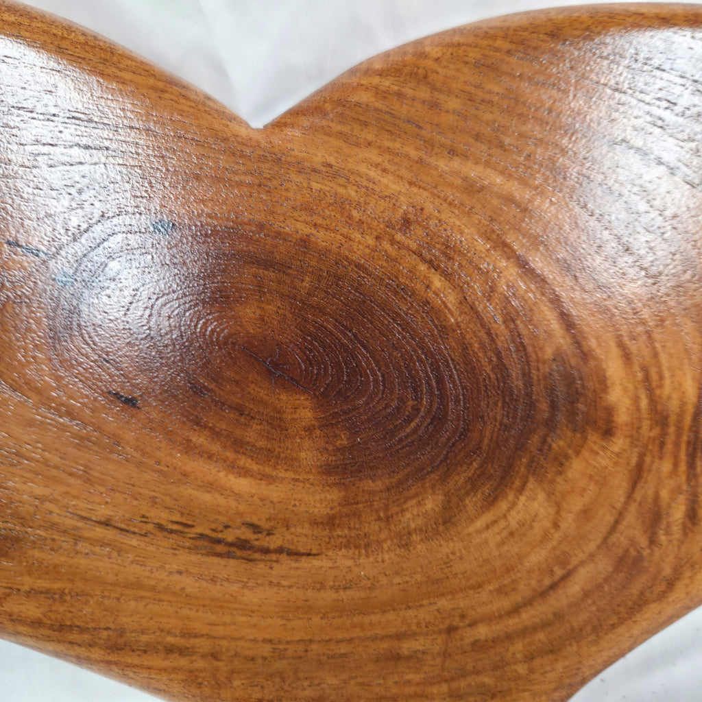 A heart-shaped hanging heart wall are with a glossy finish and visible wood grain, placed on a wrinkled white fabric background.
