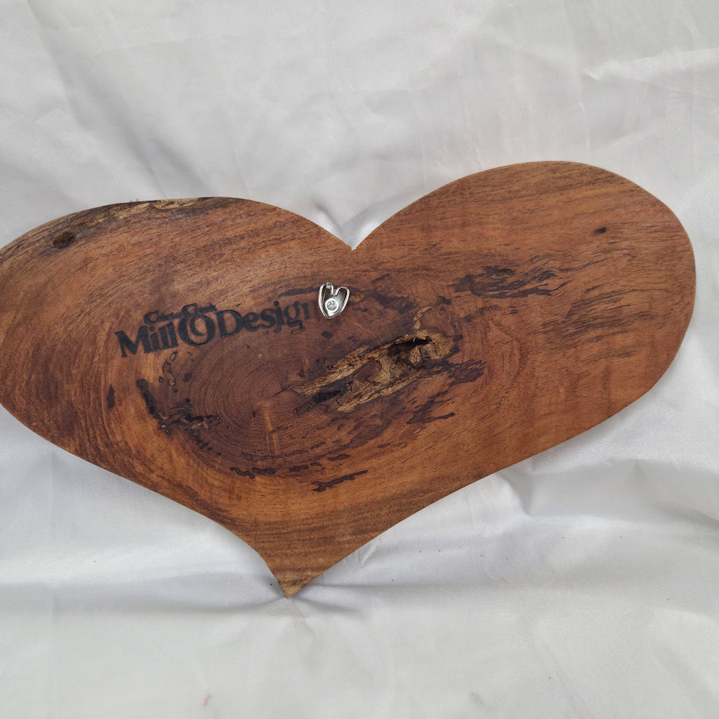 A heart-shaped hanging heart wall are with a glossy finish and visible wood grain, placed on a wrinkled white fabric background.