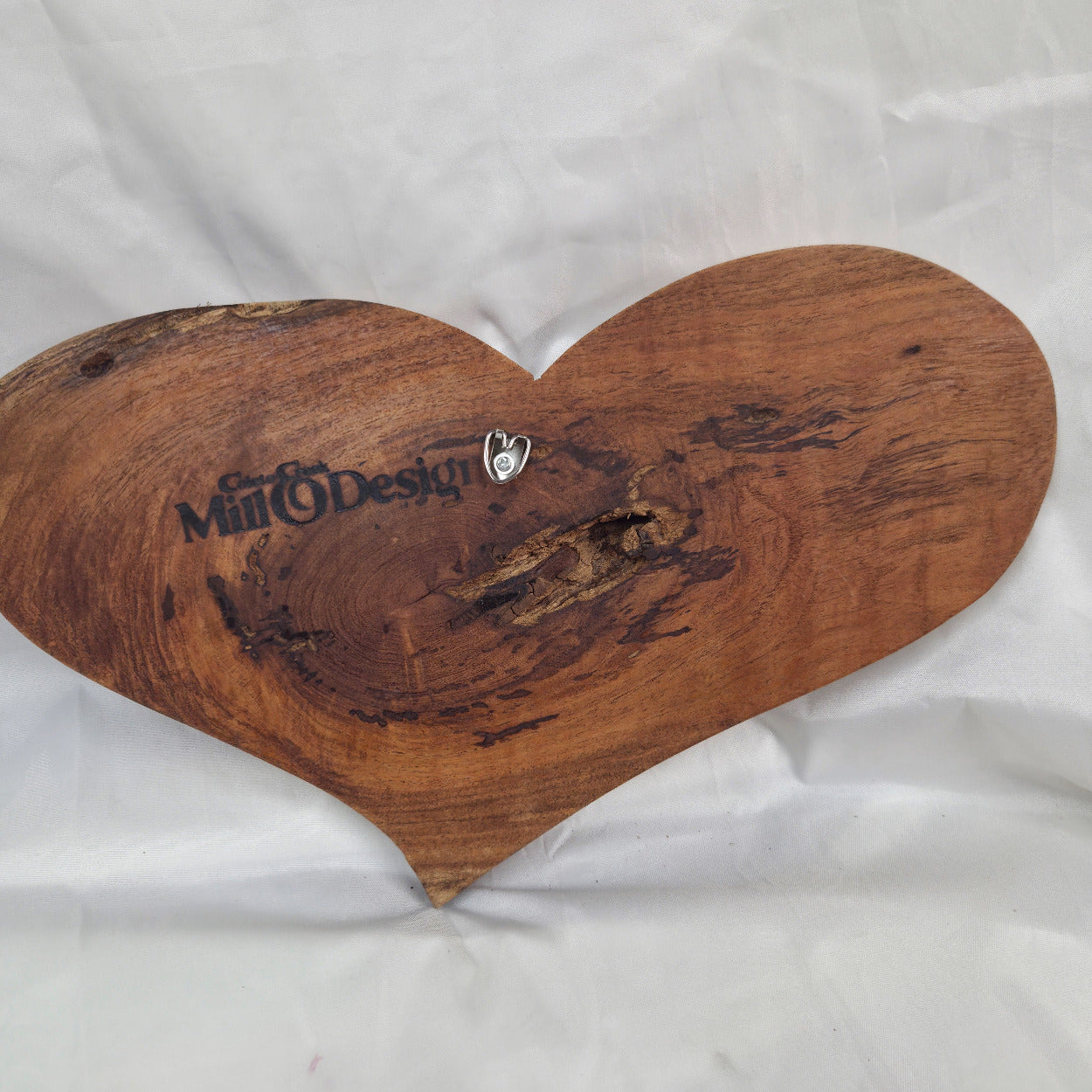 A heart-shaped hanging heart wall are with a glossy finish and visible wood grain, placed on a wrinkled white fabric background.