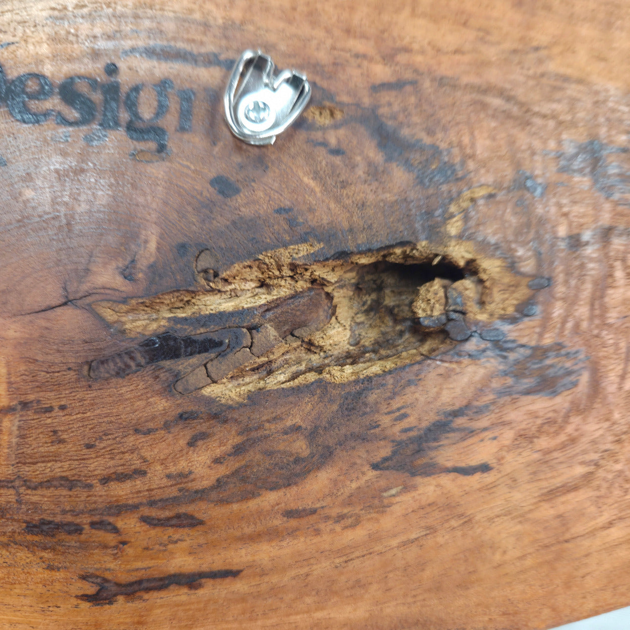 Close-up of a rustic wooden surface with prominent natural grain, a knot, and a small silver metal clip attached near the top.