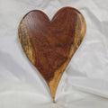 A heart-shaped wooden board with a rich dark brown center and natural light tan edges, resting on a wrinkled white fabric background.