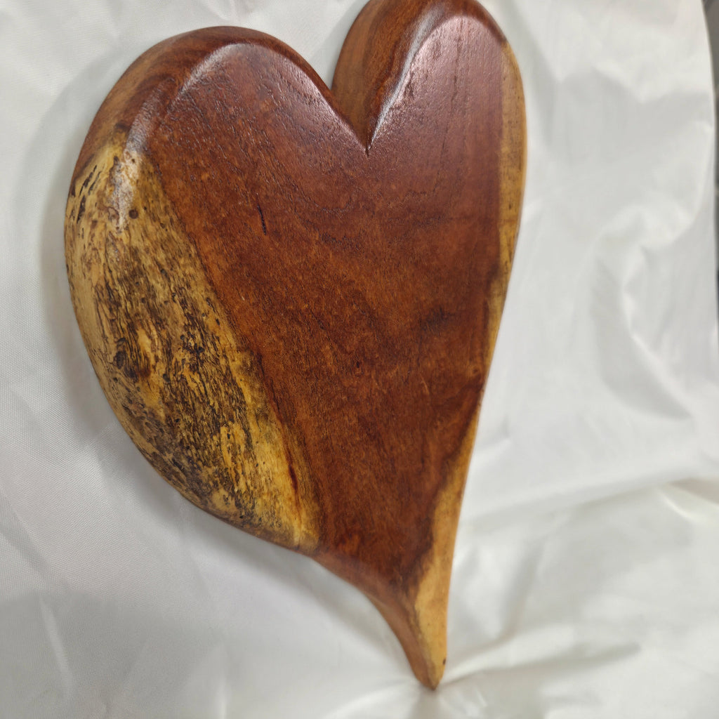 A heart-shaped wooden hanging heart wall art with a glossy dark reddish-brown finish and natural light wood edges, resting on a white fabric background.
