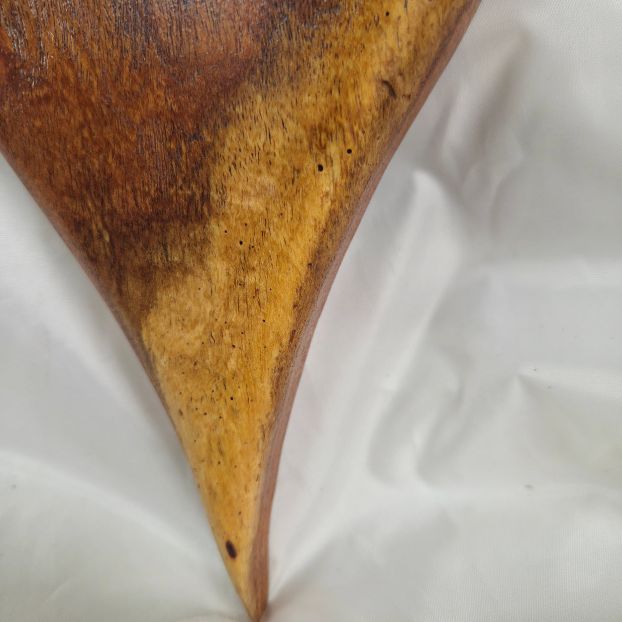 A close-up of a curved wooden object with a glossy dark brown left side and a weathered golden-yellow right side, resting on a white fabric background.