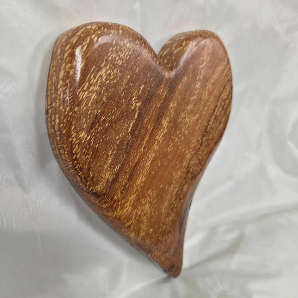 A heart-shaped White Oak Handing Heart wall art with a glossy finish and prominent natural wood grain, resting on a white fabric background.