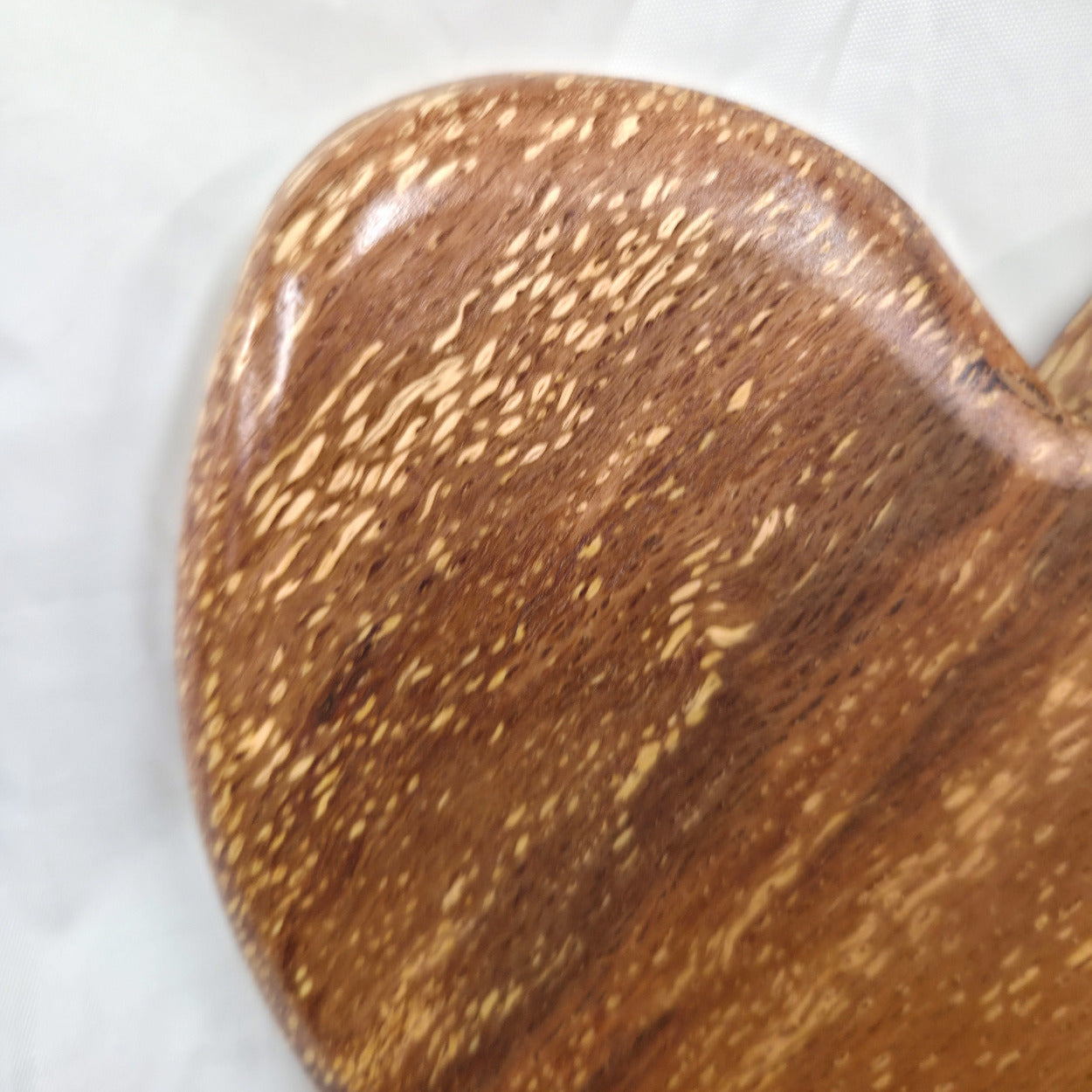 A heart-shaped White Oak Handing Heart wall art with a glossy finish and prominent natural wood grain, resting on a white fabric background.