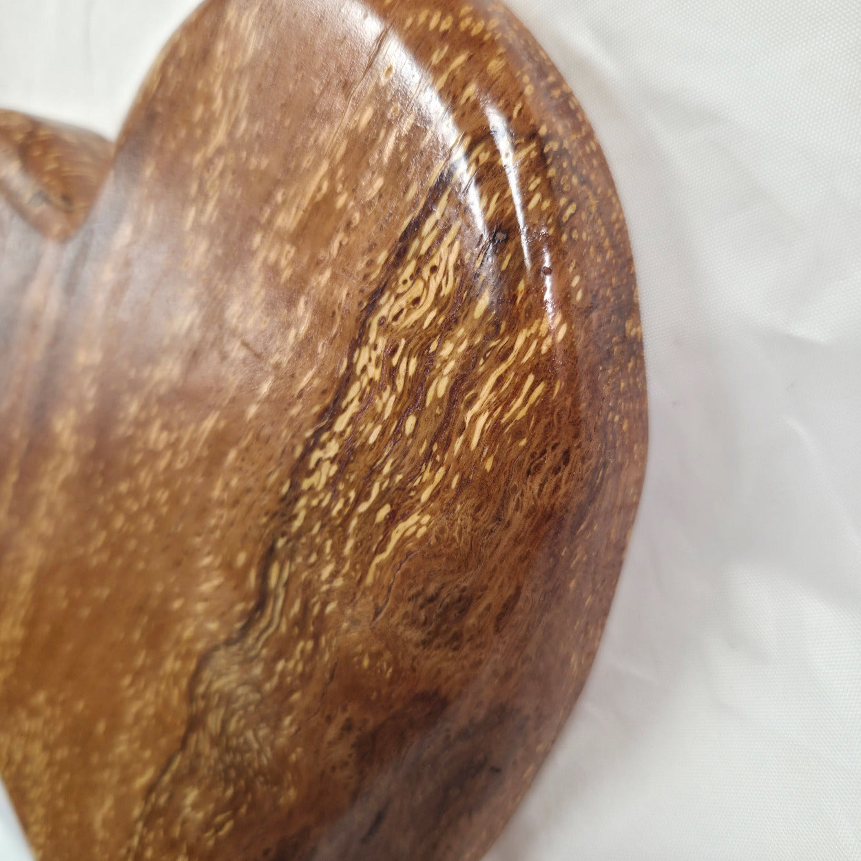 A heart-shaped White Oak Handing Heart wall art with a glossy finish and prominent natural wood grain, resting on a white fabric background.