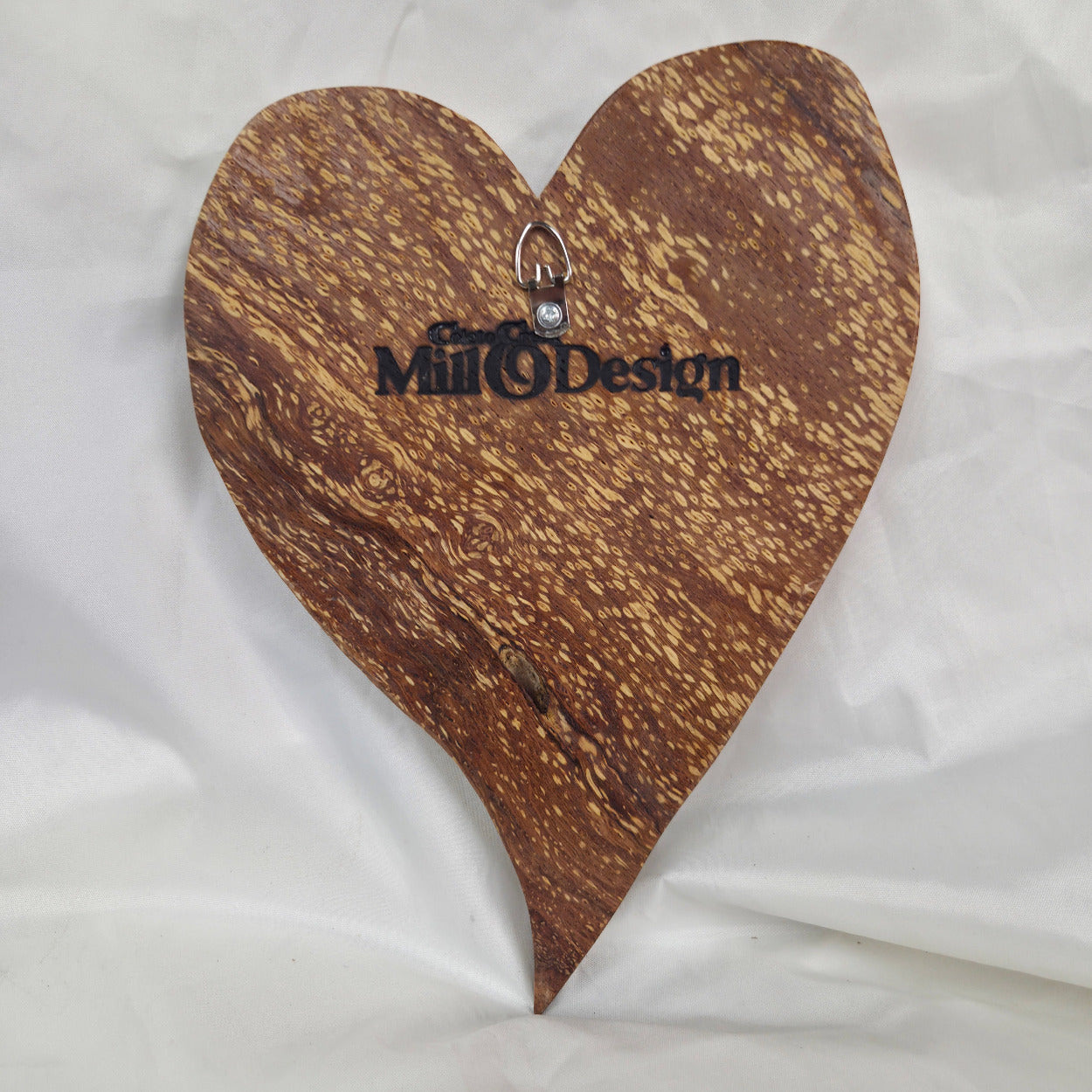 A heart-shaped White Oak Handing Heart wall art with a glossy finish and prominent natural wood grain, resting on a white fabric background.