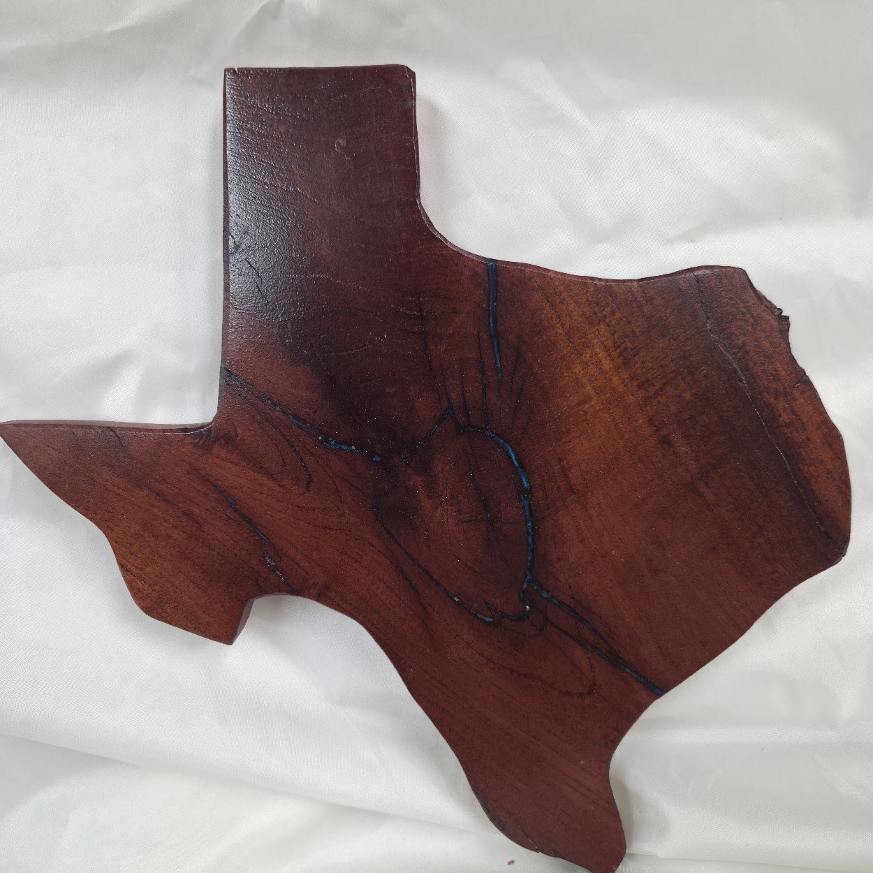 A rustic, hand-shaped wooden plaque wall art in the shape of Texas, made from mesquite wood with natural grain, dark burn marks and blue epoxy fill