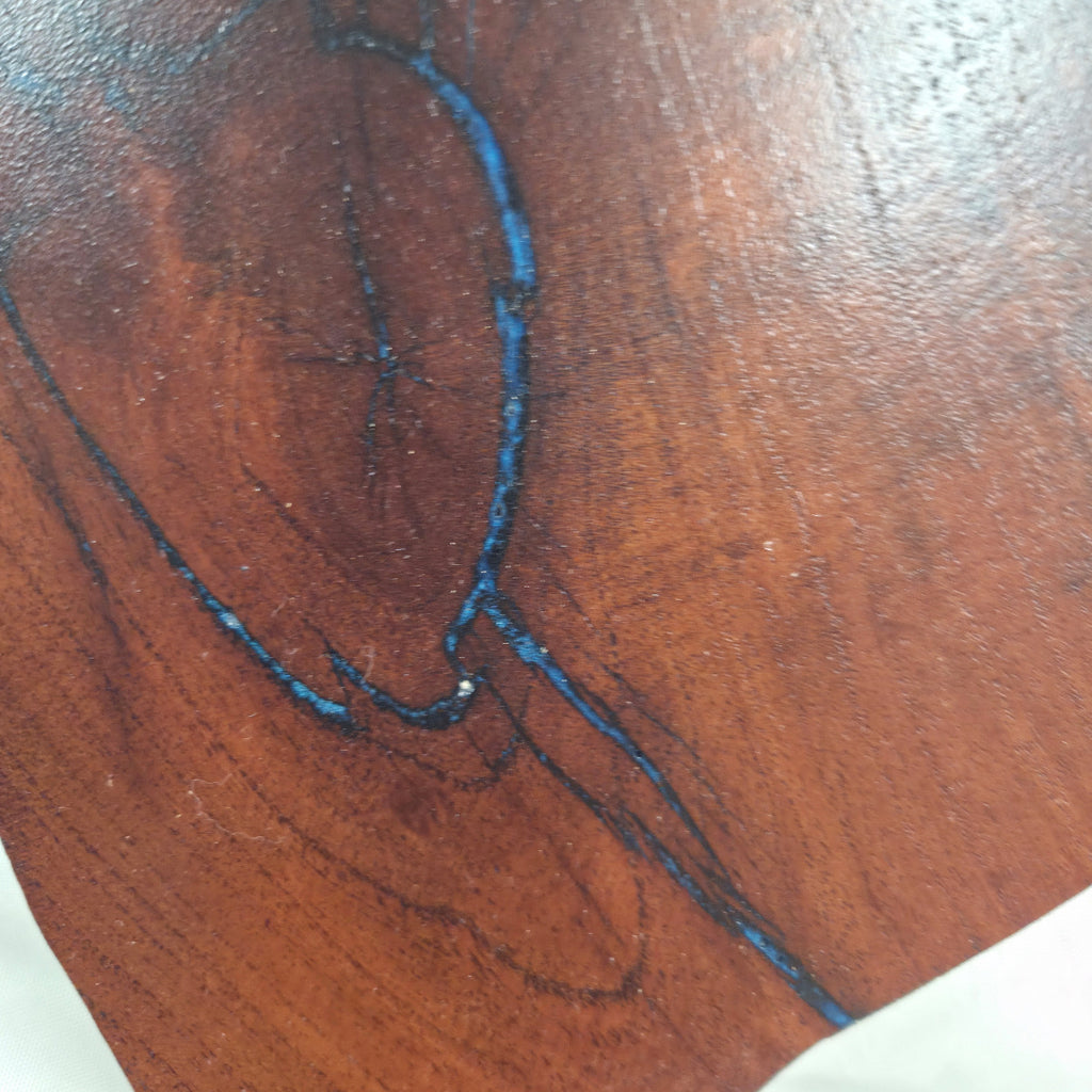 close up view A rustic, hand-shaped wooden plaque wall art in the shape of Texas, made from mesquite wood with natural grain, dark burn marks and blue epoxy fill