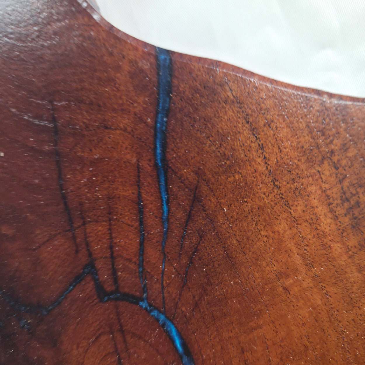 closeup A rustic, hand-shaped wooden plaque wall art in the shape of Texas, made from mesquite wood with natural grain, dark burn marks and blue epoxy fill