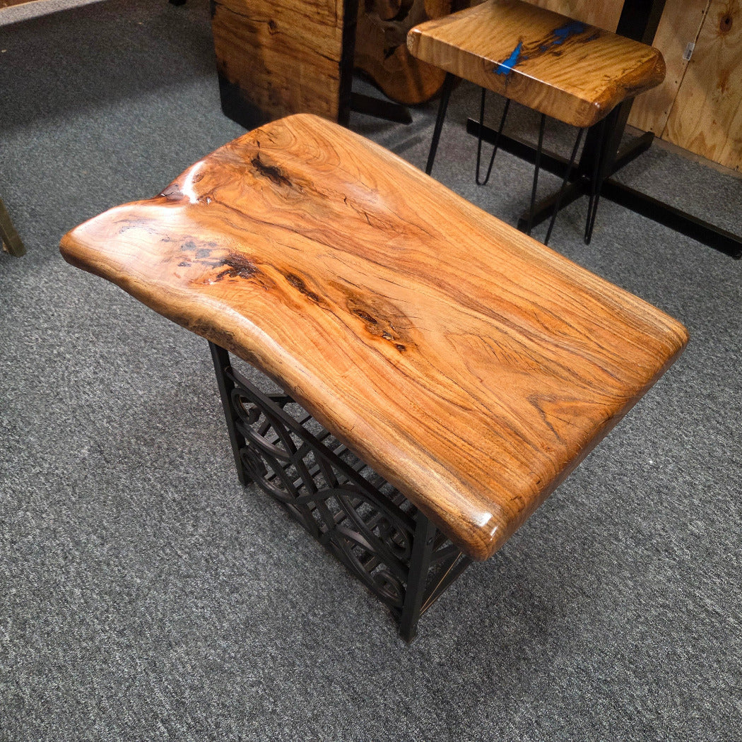 A rustic live-edge wooden table with a glossy finish and a black metal lattice base, shown on a gray carpeted floor.