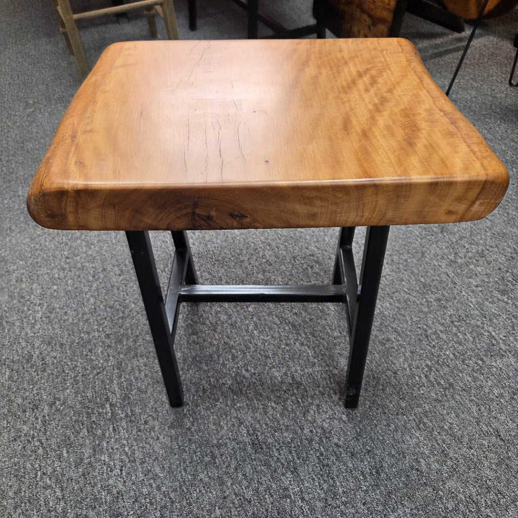 A rustic Live Oak end table with a thick, live-edge natural wood seat and a black metal frame, set on a gray carpeted floor.