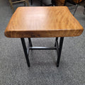 A rustic Live Oak end table with a thick, live-edge natural wood seat and a black metal frame, set on a gray carpeted floor.