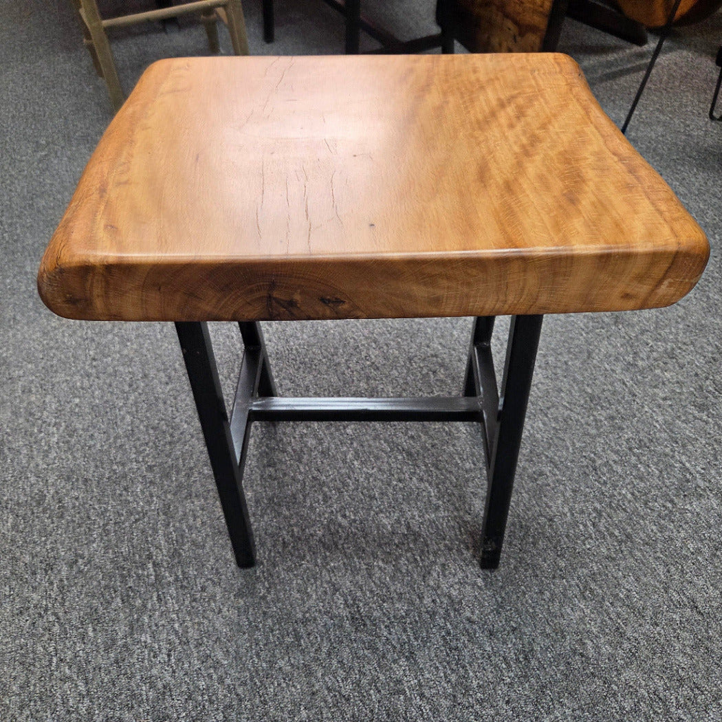 A rustic Live Oak end table with a thick, live-edge natural wood seat and a black metal frame, set on a gray carpeted floor.