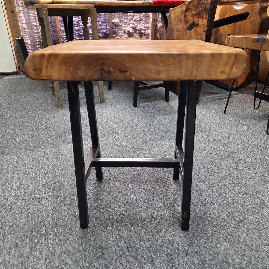 A rustic Live Oak end table with a thick, live-edge natural wood seat and a black metal frame, set on a gray carpeted floor.