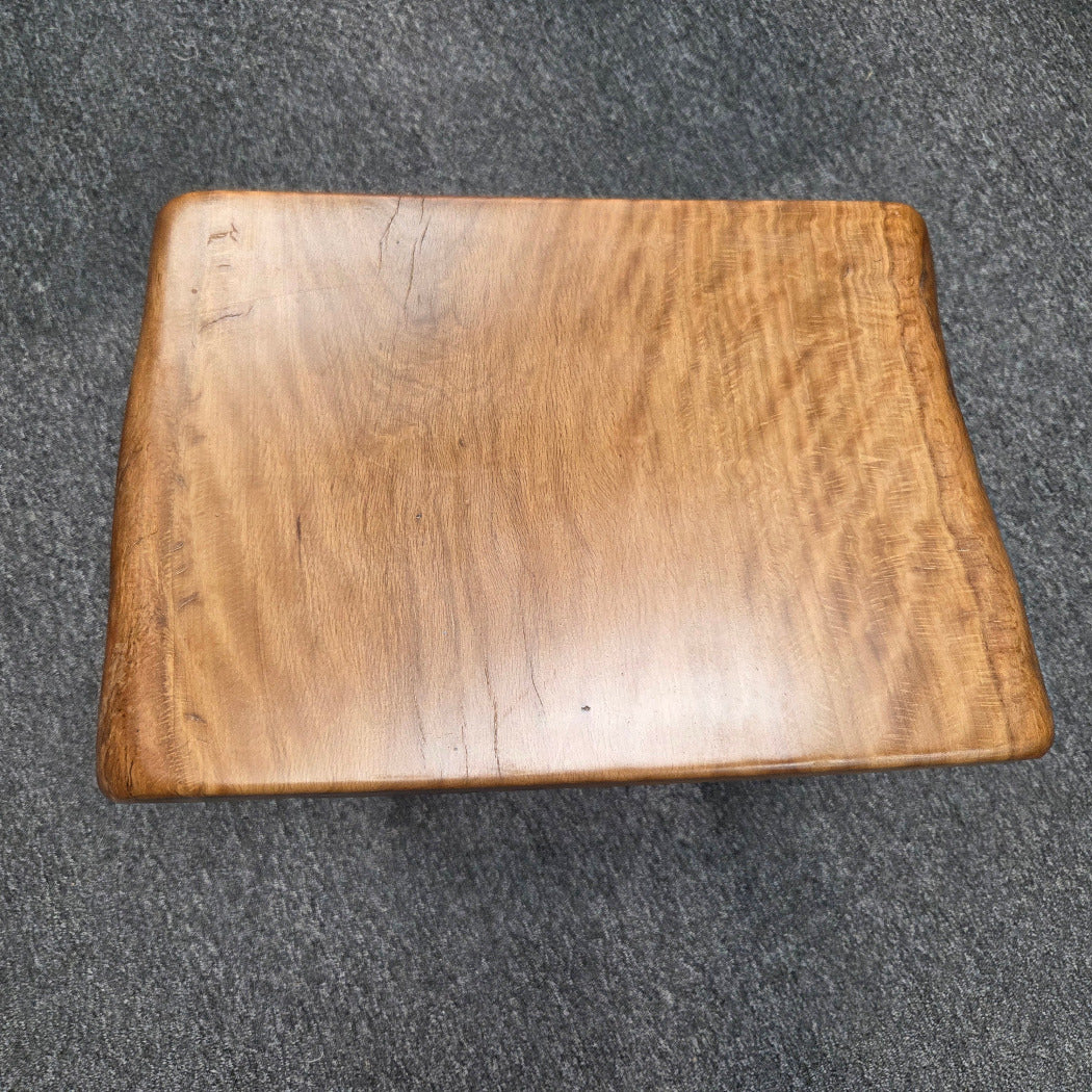 A rustic Live Oak end table with a thick, live-edge natural wood seat and a black metal frame, set on a gray carpeted floor.