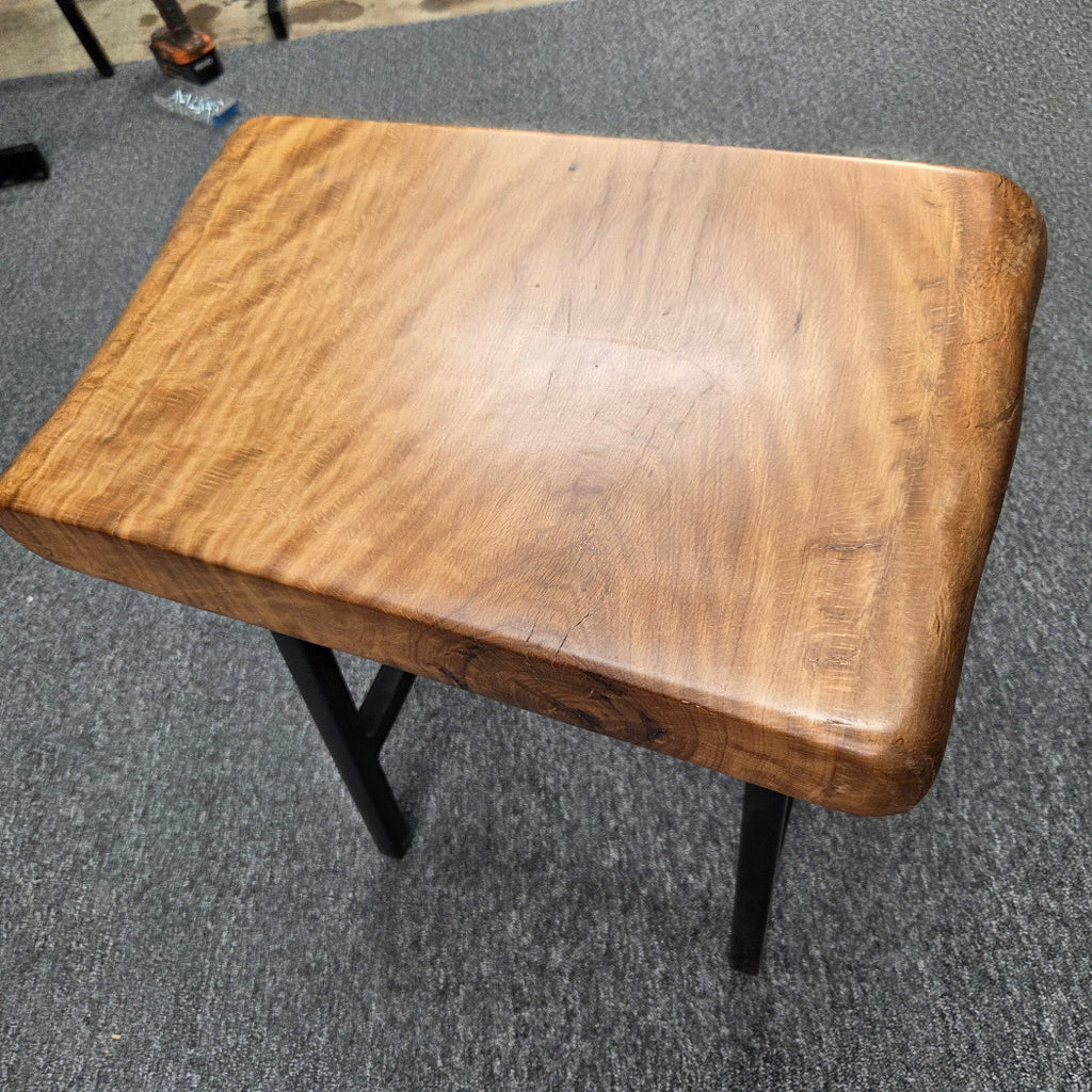 A rustic Live Oak end table with a thick, live-edge natural wood seat and a black metal frame, set on a gray carpeted floor.