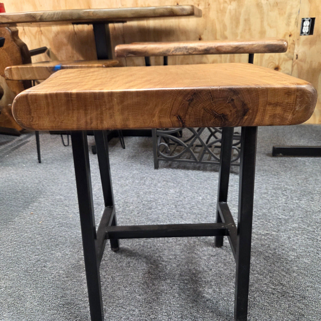 A rustic Live Oak end table with a thick, live-edge natural wood seat and a black metal frame, set on a gray carpeted floor.