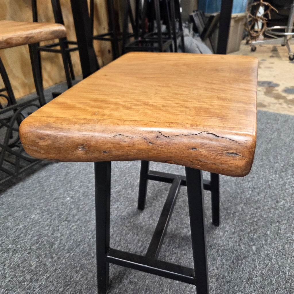 A rustic Live Oak end table with a thick, live-edge natural wood seat and a black metal frame, set on a gray carpeted floor.