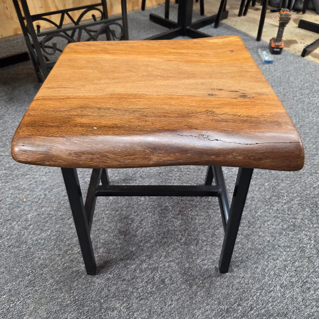 A square Live Oak end table with a live-edge natural top and black metal legs, furniture showroom setting on a gray carpet.