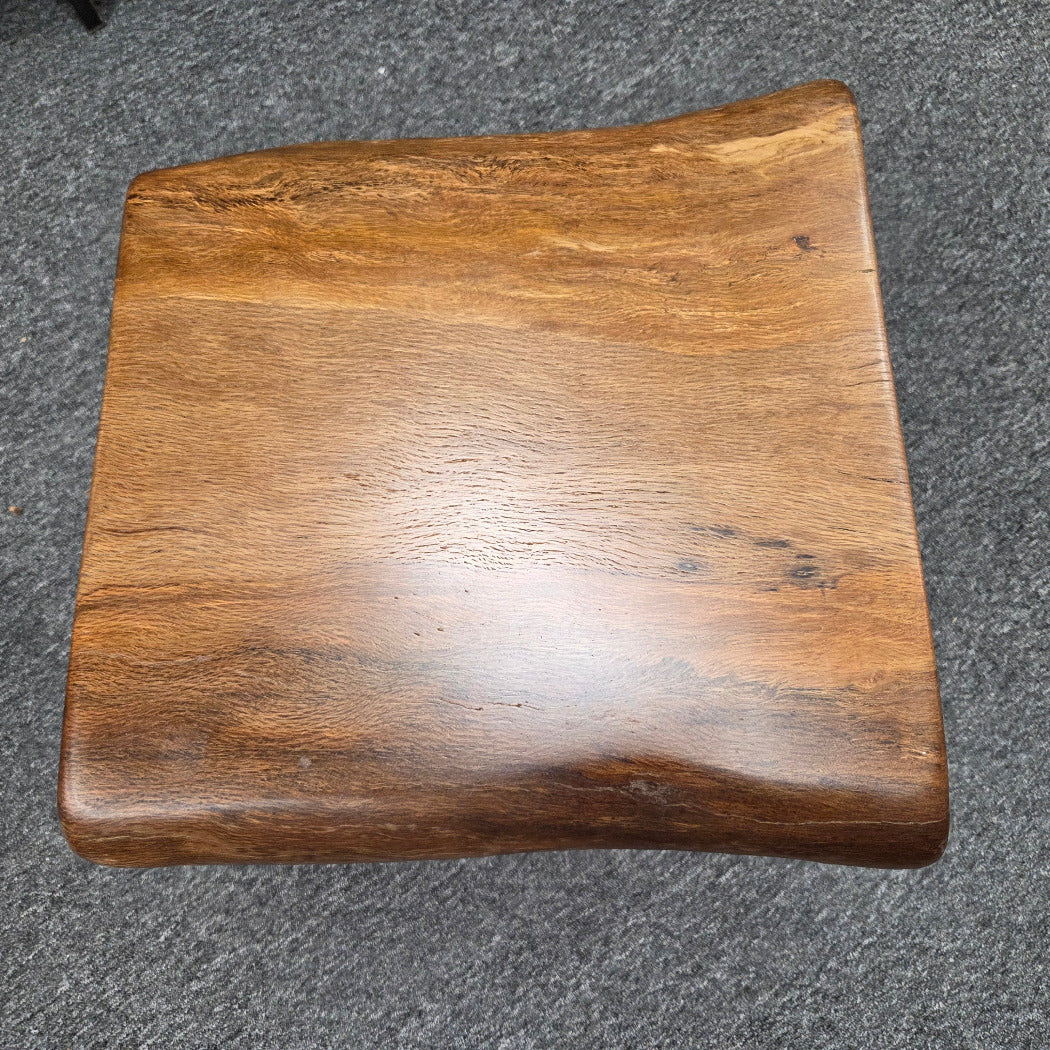 A square Live Oak end table with a live-edge natural top and black metal legs, furniture showroom setting on a gray carpet.
