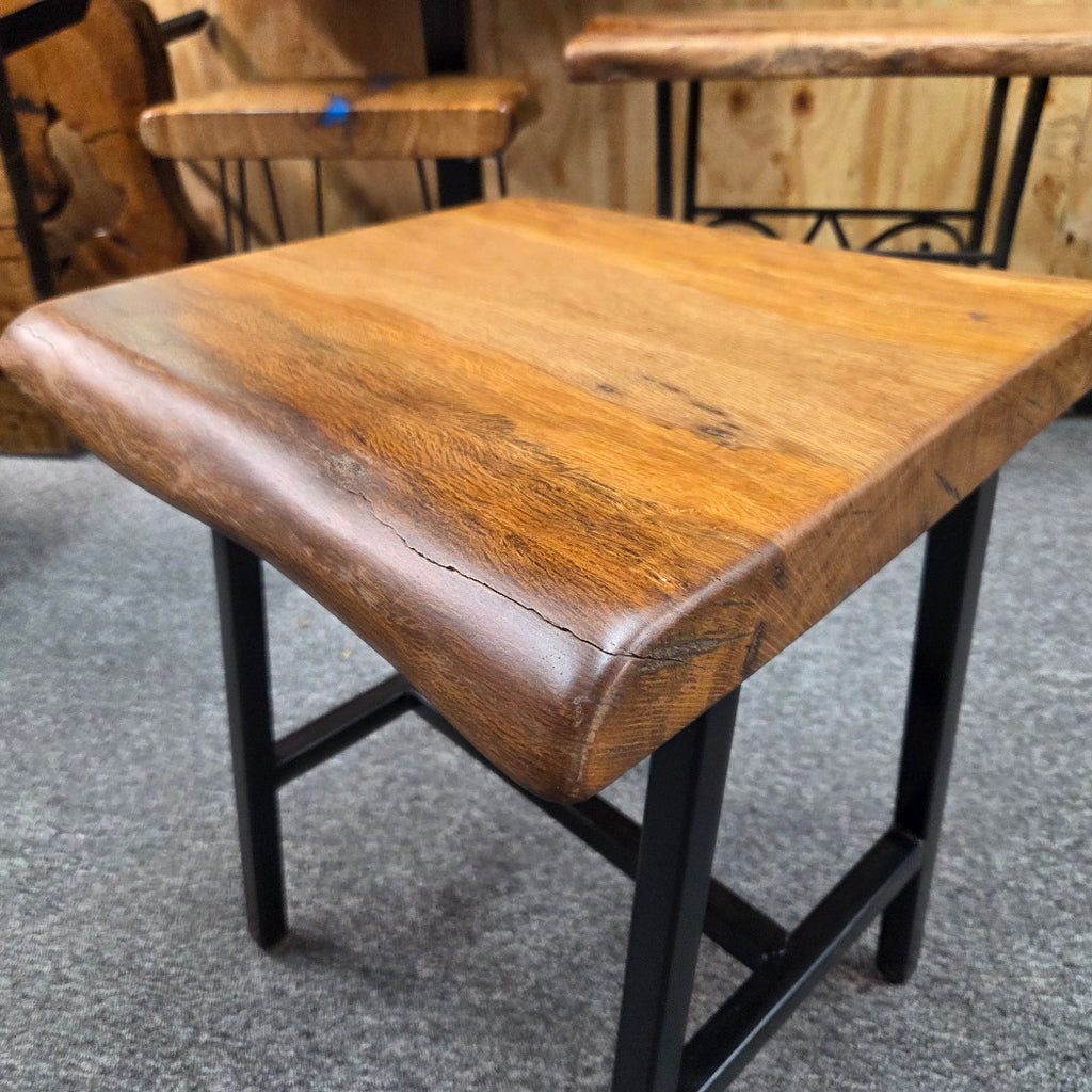 A square Live Oak end table with a live-edge natural top and black metal legs, furniture showroom setting on a gray carpet.