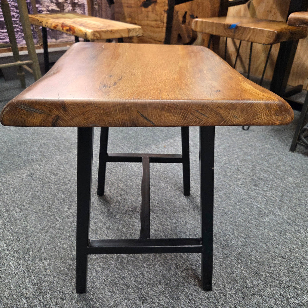 A square Live Oak end table with a live-edge natural top and black metal legs, furniture showroom setting on a gray carpet.