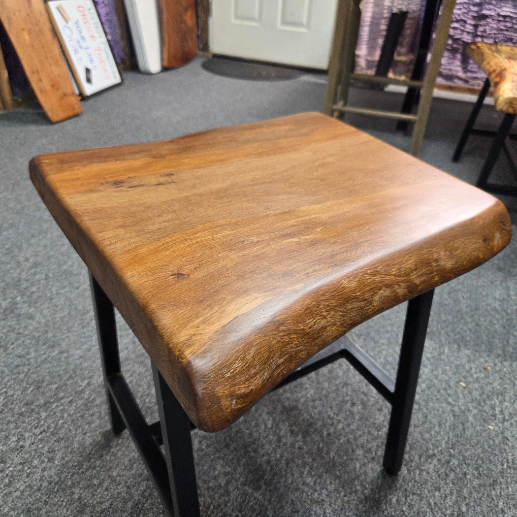A square Live Oak end table with a live-edge natural top and black metal legs, furniture showroom setting on a gray carpet.