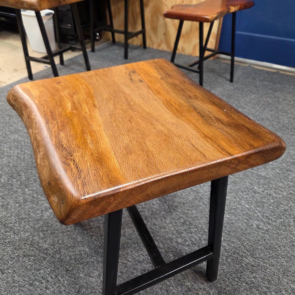 A square Live Oak end table with a live-edge natural top and black metal legs, furniture showroom setting on a gray carpet.
