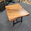 A rustic live-edge Live Oak end table with a square top and black metal legs, photographed on a gray carpeted floor.