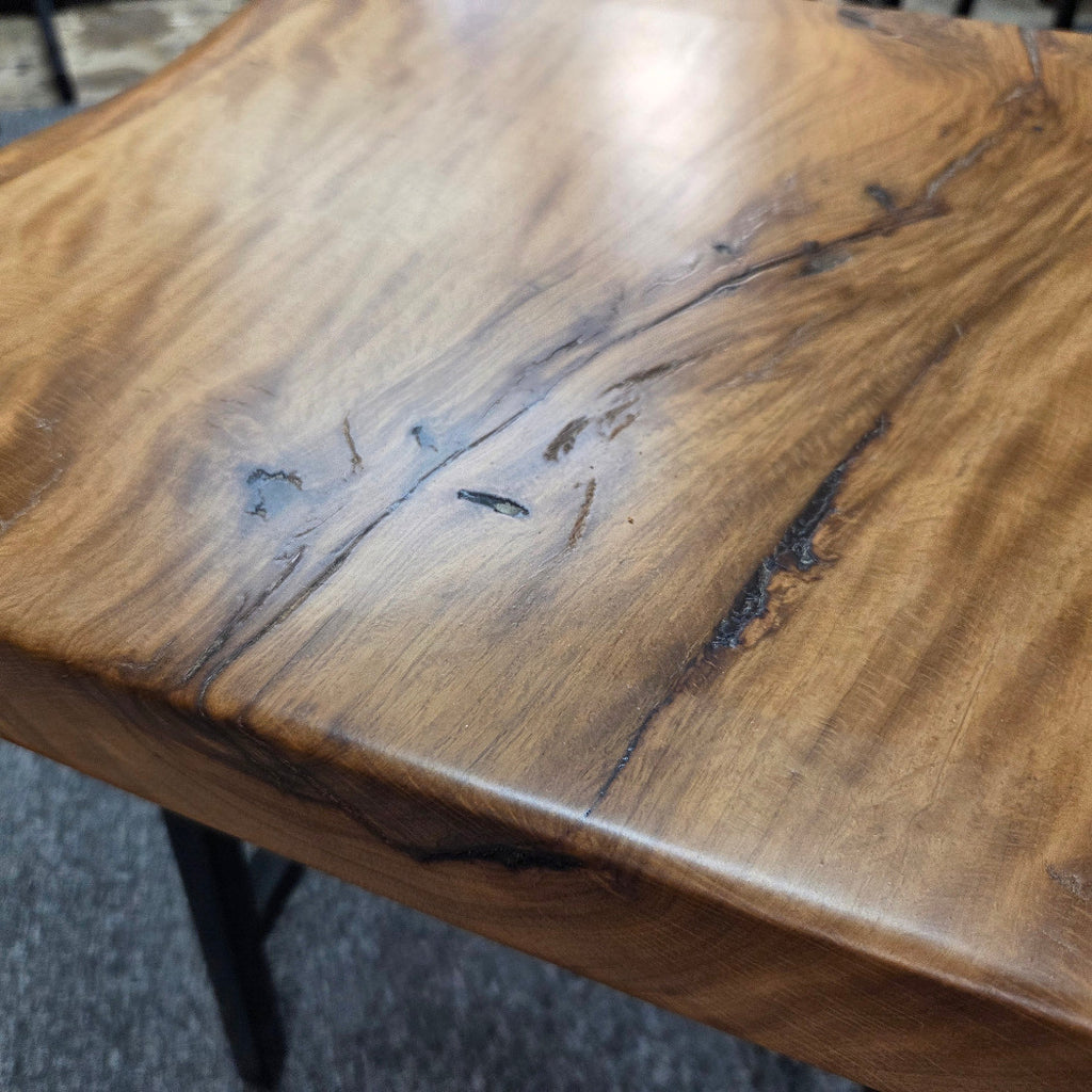 close up A rustic live-edge Live Oak end table with a square top and black metal legs, photographed on a gray carpeted floor.