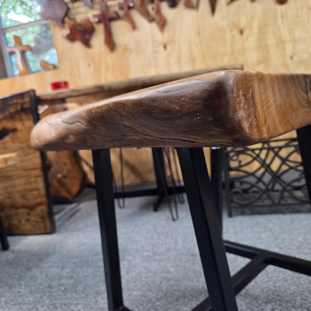 A rustic live-edge Live Oak end table with a square top and black metal legs, photographed on a gray carpeted floor.