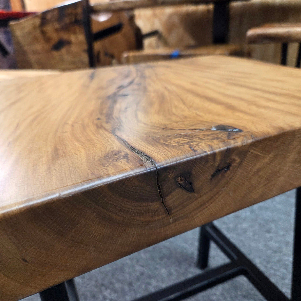A rustic live-edge Live Oak end table with a square top and black metal legs, photographed on a gray carpeted floor.